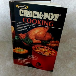 May include: A hardcover cookbook titled Rival Crock-Pot Cooking with a black cover featuring a roasted chicken, a bowl of stew, and a red slow cooker. The text includes information about the Good Housekeeping Institute and Marilyn Neill.