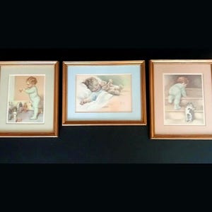 May include: A set of three framed wall art prints featuring illustrations of a young child in various activities. Each print is housed in a metallic gold frame with a colored matting, depicting scenes of a child standing, sleeping, and climbing.
