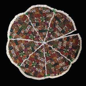 May include: A circular tree skirt featuring a patchwork design of various floral and patterned fabrics in shades of red, green, and gold. The skirt has a ruffled cream-colored border, white lace trim along the seams, and small green ribbon ties.