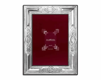 Pode incluir: Moldura de prata com um design de nó celta. A moldura tem um passe-partout de veludo vermelho e o texto "Schreiner & Co.  Estabelecido em 1877  Presentes elegantes  Qualidade excepcional" está impresso no passe-partout.