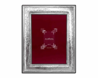 Pode incluir: Moldura de prata com textura martelada e detalhes florais ornamentados. A moldura tem um interior vermelho escuro e um verso preto. O texto "Silver Brand" é visível. Uma peça decorativa para exibir fotos ou obras de arte.
