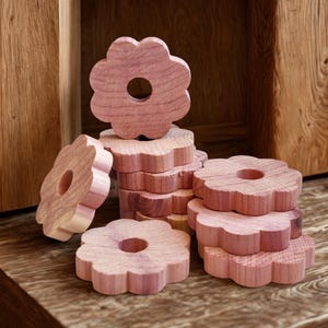 May include: A collection of flower-shaped cedar wood blocks. The blocks are a light reddish-brown color and have a hole in the center. They are stacked and scattered on a wooden surface, with a wooden background.