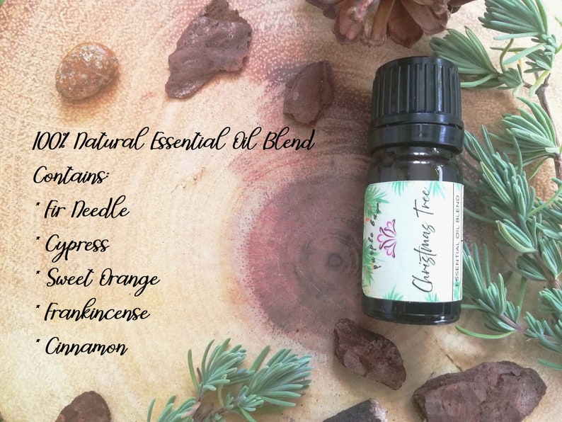 May include: A small, dark glass bottle of "Christmas Tree" essential oil blend. The label lists ingredients: fir needle, cypress, sweet orange, frankincense, and cinnamon. The bottle sits on a wooden surface with sprigs of greenery and bark.