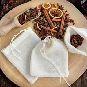 May include: A wooden scoop and small muslin bags filled with spices, including star anise, cinnamon sticks, and dried orange slices, are arranged on a wooden serving board. The scene is set against a rustic wooden background, suggesting a focus on natural ingredients.