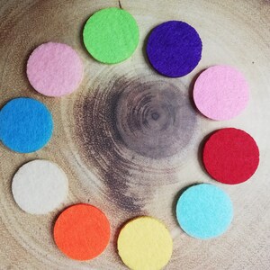 May include: Nine round felt diffusers in various colours, including pink, blue, green, yellow, orange, and red, arranged in a circle on a wooden surface.