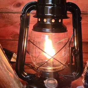 May include: A black metal kerosene lantern with a glass globe and a wire cage. The lantern is lit and casting a warm glow.