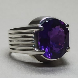 May include: A silver ring with a large, oval-shaped amethyst gemstone. The ring has a textured band.