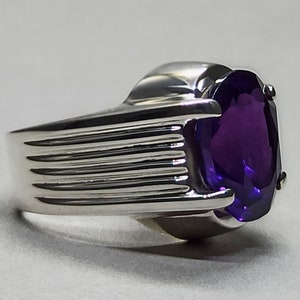 May include: A silver ring with a large, oval-shaped amethyst gemstone. The band of the ring has a textured design.