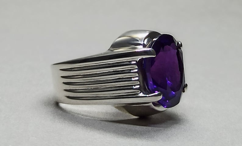 May include: A silver ring with a large, oval-shaped amethyst gemstone. The band of the ring has a textured design.