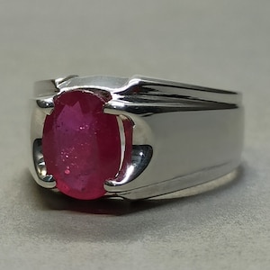 May include: A silver ring with a large, oval-shaped ruby gemstone. The ruby is a deep red color and is set in a simple, modern design.