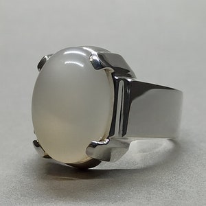 May include: A silver ring with a large, oval-shaped white gemstone set in a prong setting.