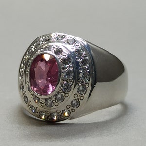 May include: A silver ring with a pink oval gemstone surrounded by a double row of smaller clear gemstones.