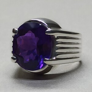 May include: A silver ring with a large, oval-shaped amethyst gemstone. The ring has a textured band.