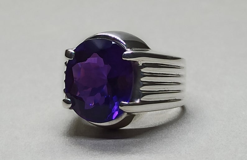 May include: A silver ring with a large, oval-shaped amethyst gemstone. The ring has a textured band.
