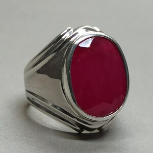 Puede incluir: Un anillo de plata con una piedra preciosa grande, de forma ovalada y de color rojo intenso.