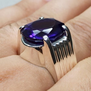 May include: A silver ring with a large, oval-shaped amethyst gemstone. The ring has a textured band.