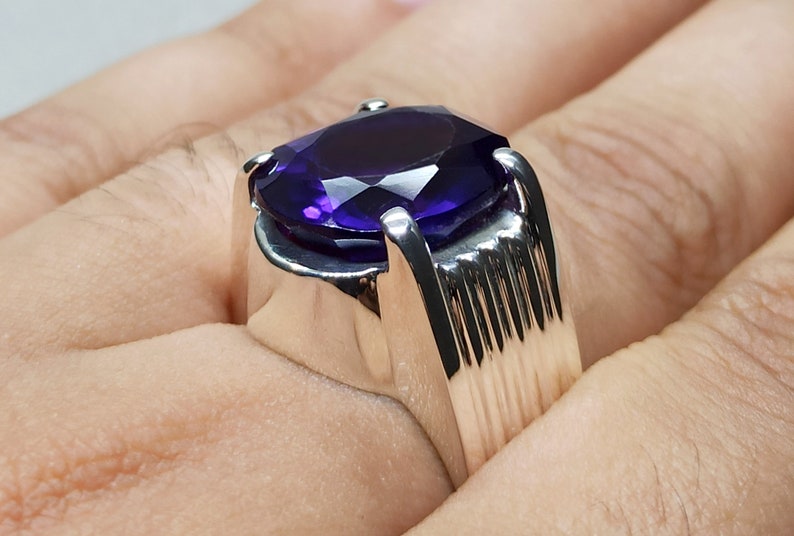 May include: A silver ring with a large, oval-shaped amethyst gemstone. The ring has a textured band.