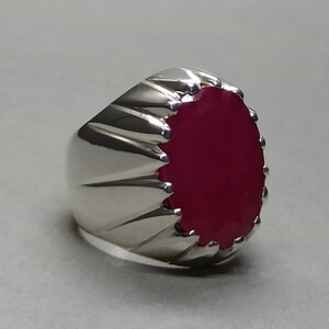 May include: A silver ring with a large, oval-shaped, deep red gemstone set in the center. The ring band has a textured, ridged design.