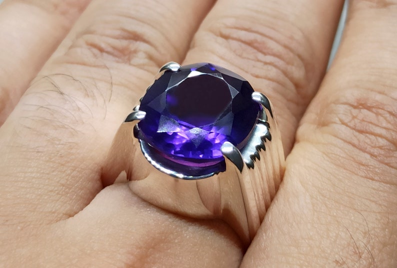 May include: A silver ring with a large, round, deep purple amethyst gemstone. The ring has a thick band with a textured design.
