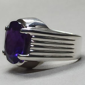 May include: A silver ring with a large, oval-shaped amethyst gemstone. The band of the ring has a textured, ridged design.
