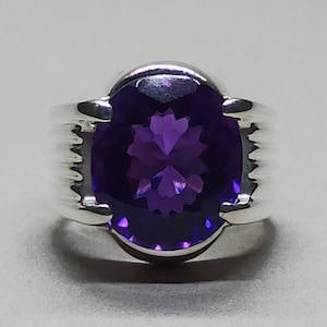 May include: A silver ring with a large, oval-shaped amethyst gemstone. The ring has a textured band.