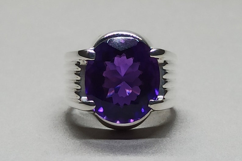 May include: A silver ring with a large, oval-shaped amethyst gemstone. The ring has a textured band.