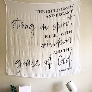 May include: A white canvas tapestry with black text that reads "The child grew and became strong in spirit, filled with wisdom and the grace of God. Luke 2:40"