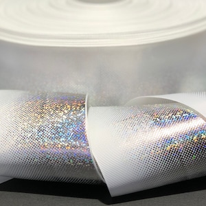 May include: A roll of white iridescent ribbon with a subtle textured pattern. The ribbon is folded and rolled, showing the iridescent finish.