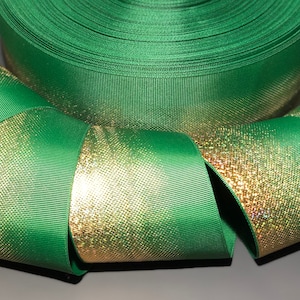 May include: Green and gold ribbon with a shimmery gold finish. The ribbon is folded and rolled up, showing the texture and color of the fabric.