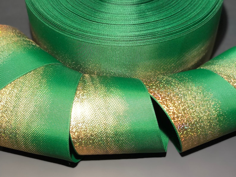 May include: Green and gold ribbon with a shimmery gold finish. The ribbon is folded and rolled up, showing the texture and color of the fabric.