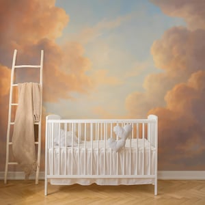 May include: A white crib with bedding and heart-shaped pillows is set against a mural of a cloudy sky in shades of orange, peach, and blue. A wooden ladder with a beige blanket leans against the wall, adding a cozy touch to the nursery.