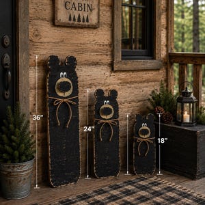 May include: Three black wooden bear-shaped signs with distressed edges, white eyes, and tan circular snouts. Each bear features a tied jute rope bow around the neck. The heights are marked as 36 inches, 24 inches, and 18 inches respectively.