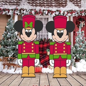 May include: Two red and green Christmas nutcracker figurines of Mickey Mouse and Minnie Mouse. Mickey is wearing a red and green uniform with a black hat and a gold belt. Minnie is wearing a red and green uniform with a black hat and a gold belt. She has a red bow on her head.