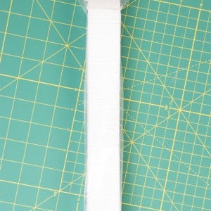 May include: White elastic strap for purse making, packaged on a white card with the text "by Annie.com Purse Parts".