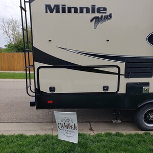 May include: A white and brown camper with the text "Minnie Plus" on the side. A sign in front of the camper says "Welcome to our Camper The T-setter's Est. 2021".
