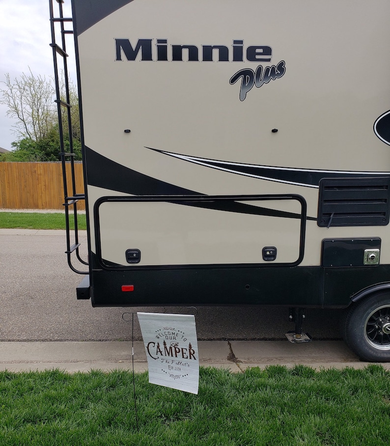 May include: A white and brown camper with the text "Minnie Plus" on the side. A sign in front of the camper says "Welcome to our Camper The T-setter's Est. 2021".