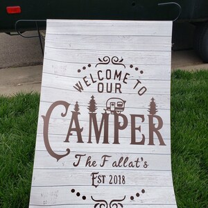 May include: White wooden sign with brown text that reads "Welcome to our Camper The Fallat's Est 2018". The sign has a stylized camper icon and a decorative flourish.