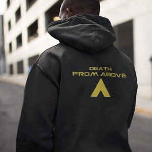 Puede incluir: Sudadera con capucha negra con el texto "DEATH FROM ABOVE" y un gráfico de triángulo dorado en la espalda.