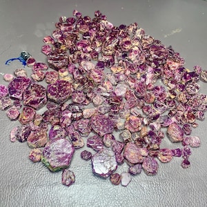 Puede incluir: Un conjunto de gemas en bruto, sin tallar, de diversos tamaños y formas. Las piedras muestran un tono púrpura intenso con inclusiones cristalinas más claras. La disposición sugiere un enfoque en la belleza natural y sin refinar.