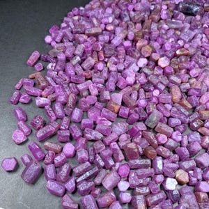 Peut inclure: Un grand tas de petits cristaux de rubis roses bruts. Les cristaux sont de formes et de tailles variées, certains étant plus allongés que d'autres. Les cristaux sont tous d'une couleur rose foncé, certains ayant une teinte légèrement plus foncée que d'autres.