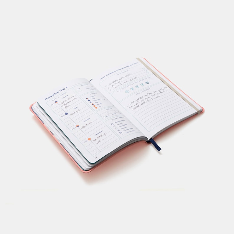 May include: A pink and blue journal with the words "Ramadan Day 1" on the cover. The journal has a daily planner section and a gratitude section. The gratitude section has the text "I am grateful to have been given so much, but I still need more of your forgiveness."