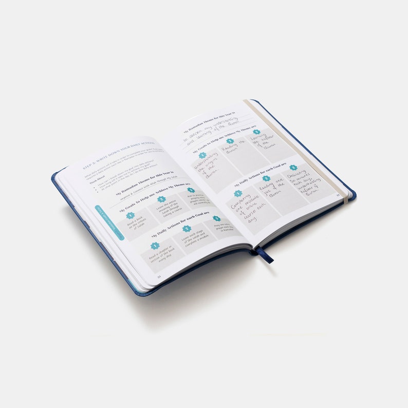 May include: An open blue journal with a white interior. The pages are filled with handwritten notes and lists. The journal is titled "My Ramadan Themes for this year is..." and "My Daily Actions for each Goal are..."