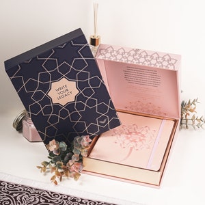 May include: A pink and gold gift box with a navy blue box on top. The navy blue box has a gold geometric pattern and the text "Write Your Legacy". The pink box has a gold geometric pattern and the text "Write Your Legacy" on the inside.