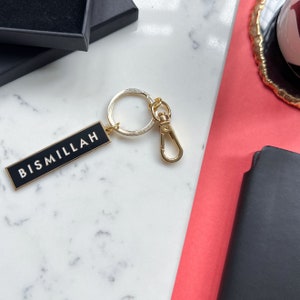 May include: A gold keychain with a black rectangular tag that says "Bismillah" in white lettering.