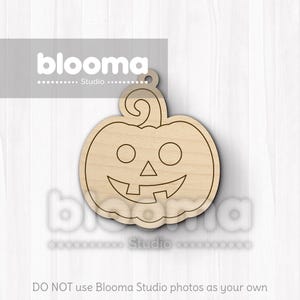 May include: A wooden pumpkin-shaped cutout with a carved smiling face and a curly stem. The cutout has a hole at the top for hanging and is made of light-colored wood. The text "blooma Studio" is visible in the image.