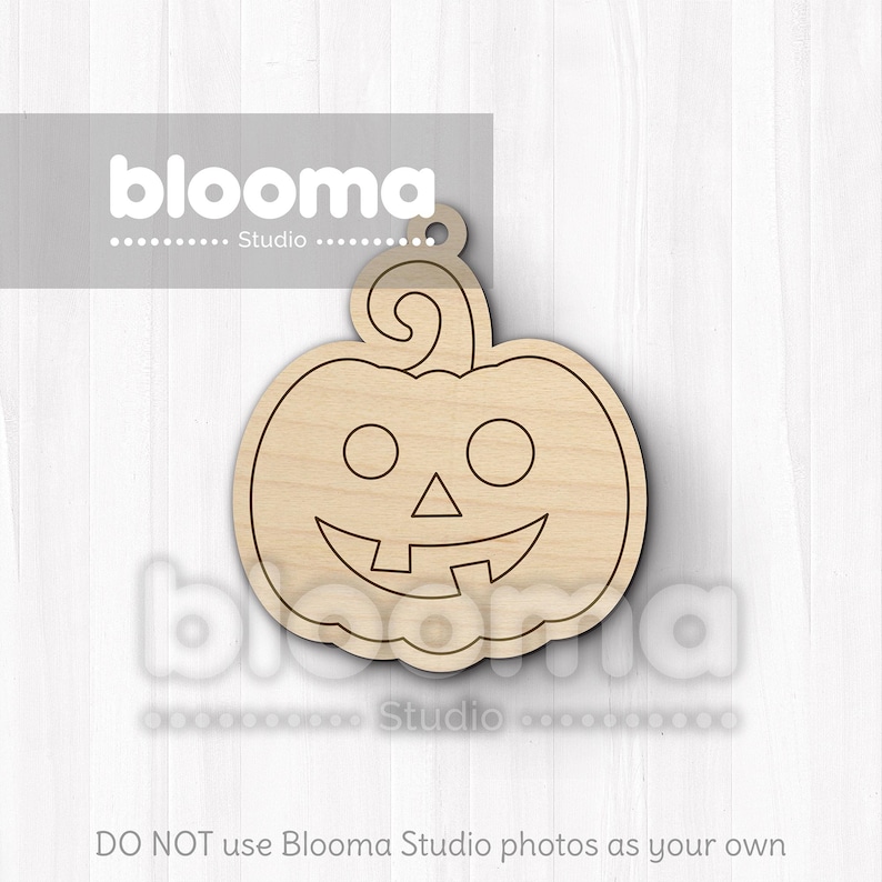 May include: A wooden pumpkin-shaped cutout with a carved smiling face and a curly stem. The cutout has a hole at the top for hanging and is made of light-colored wood. The text "blooma Studio" is visible in the image.