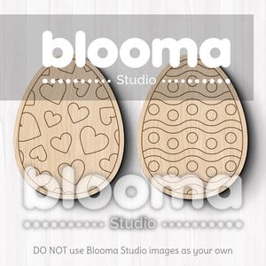 May include: Two wooden Easter egg cutouts, one with a heart pattern and the other with a wavy line and circle pattern. The text "blooma Studio" is printed on the image.