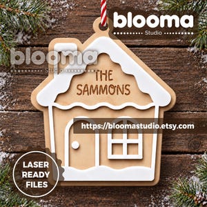 Pode incluir: Um ornamento de madeira castanho-claro em forma de casa com detalhes brancos em camadas no telhado e na base. O texto THE SAMMONS está gravado no centro. O ornamento apresenta uma chaminé, uma porta e uma janela, pendurado por um cordão vermelho e branco.