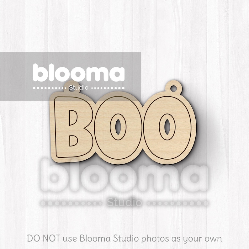May include: A wooden cutout spelling "BOO" with a small hole at the top for hanging. The letters are outlined in a dark brown color. The word "blooma" is printed in white above and below the cutout.