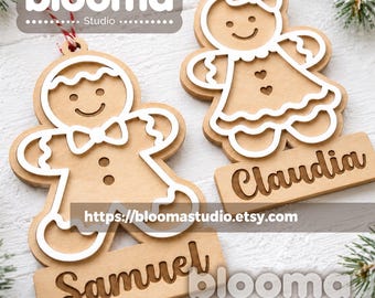 May include: Two light brown wooden gingerbread ornaments with white painted outlines. One ornament features a bow tie and the name Samuel, while the other features a bow and the name Claudia. Both ornaments have red and white string loops for hanging.